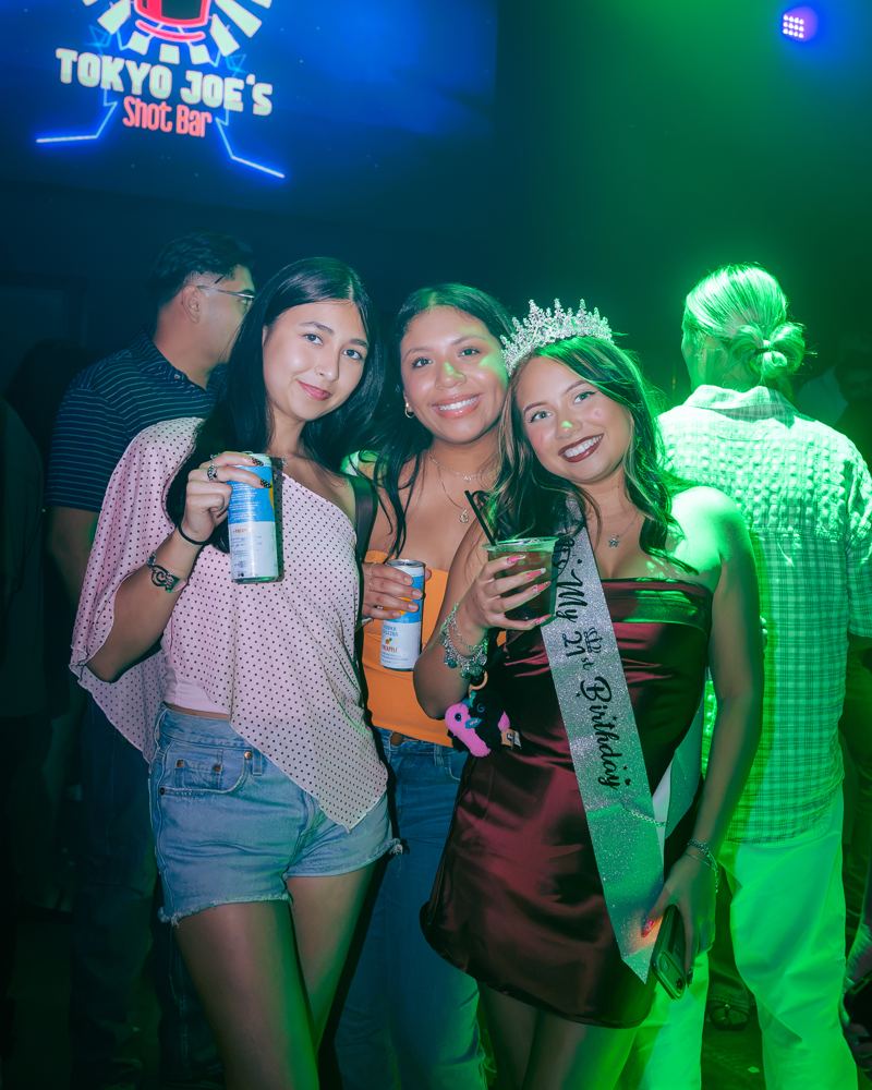 A birthday girl in a sash and tiara with two friends under the Tokyo Joe's sign