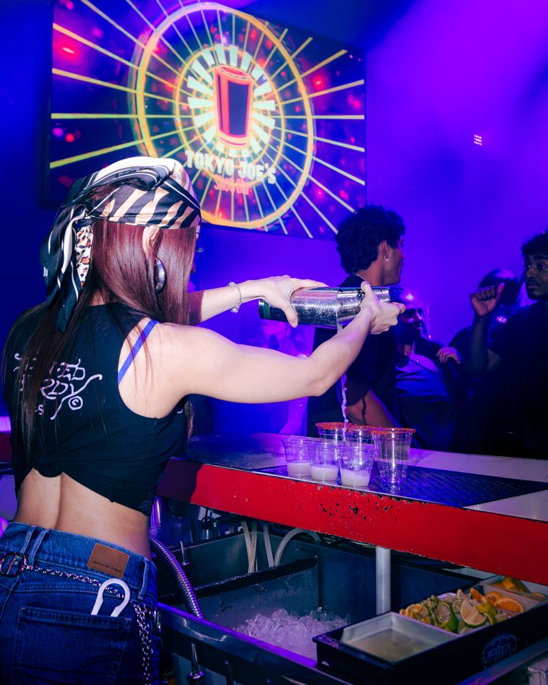 Bartender pouring a row of shots under the Tokyo Joe's sunburst screen